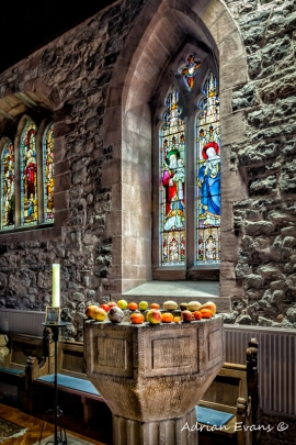 fresh fruit on the ancient font with beautiful stained glass windows in an ancient Welsh church, north Wales UK